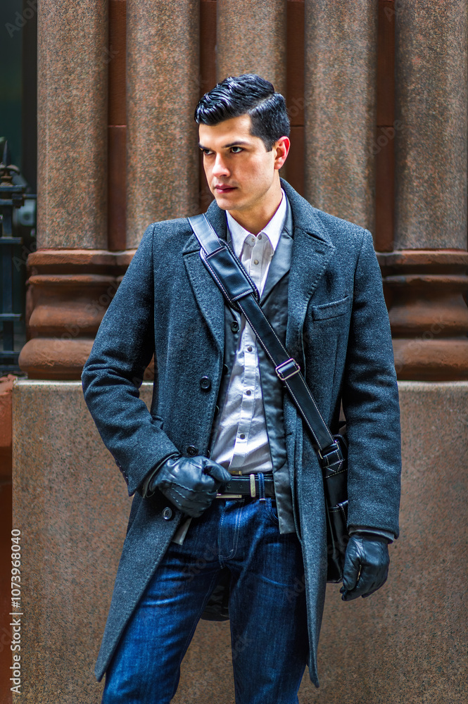 A well-dressed man stands confidently in front of a stone column, wearing a dark overcoat and gloves with a crossbody bag. His poised stance and stylish attire suggest a sense of urban sophistication.