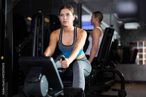 Active young woman engaged in arm workout on cable type fitness equipment in exercise room