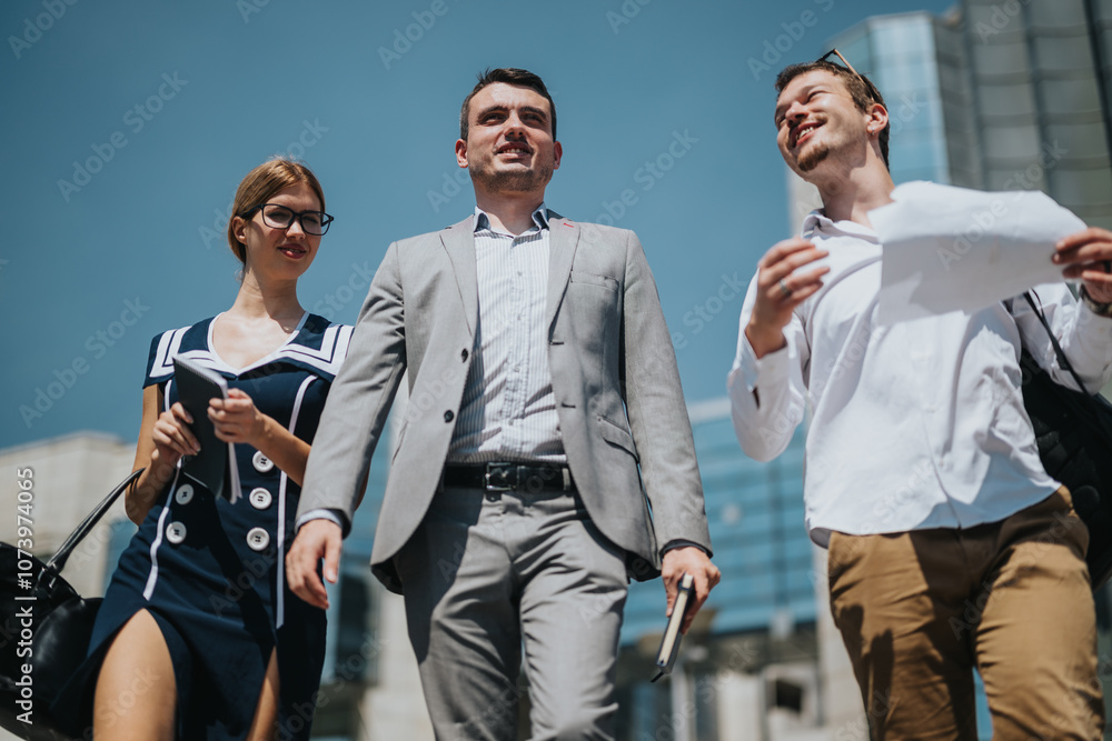 Fototapeta premium Group of three young professionals walking confidently through a modern cityscape, symbolizing teamwork, leadership, and success in a corporate environment.