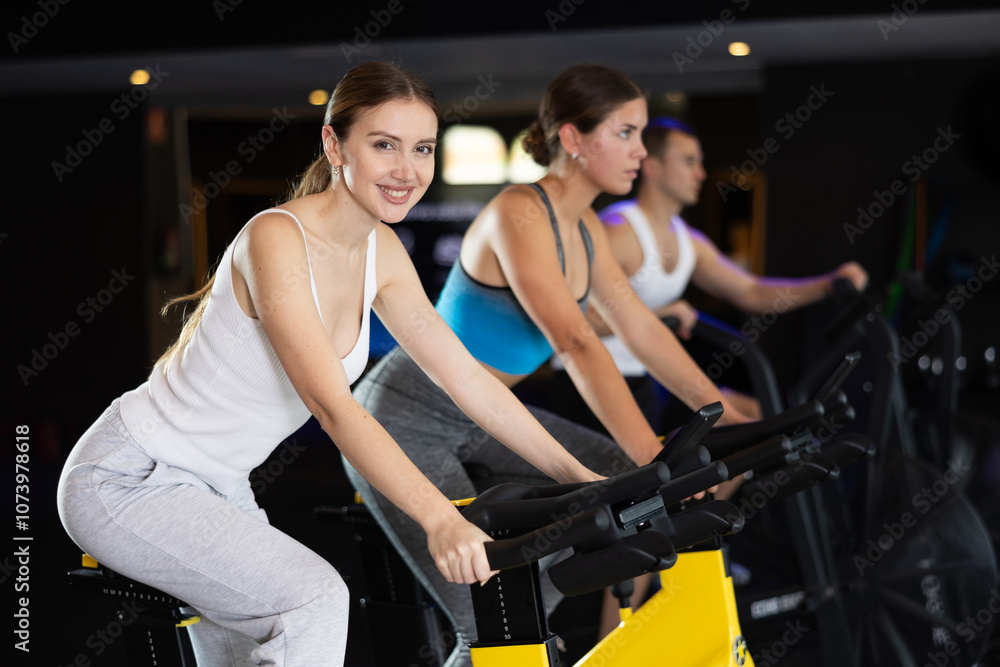 Smiling young girl training with spin bike in fitness hall during full-body workout Smiling young girl training with spin bike in fitness hall during full-body workout