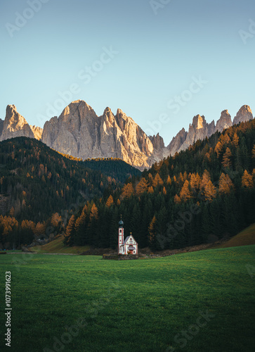 Charming alpine chapel in a mountain meadow surrounded by pines and Dolomitic mounatins at sunset photo