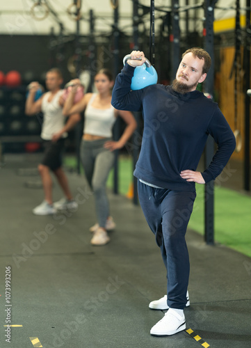 Strong young man practicing with kettlebell in exercise room during weight training classes photo