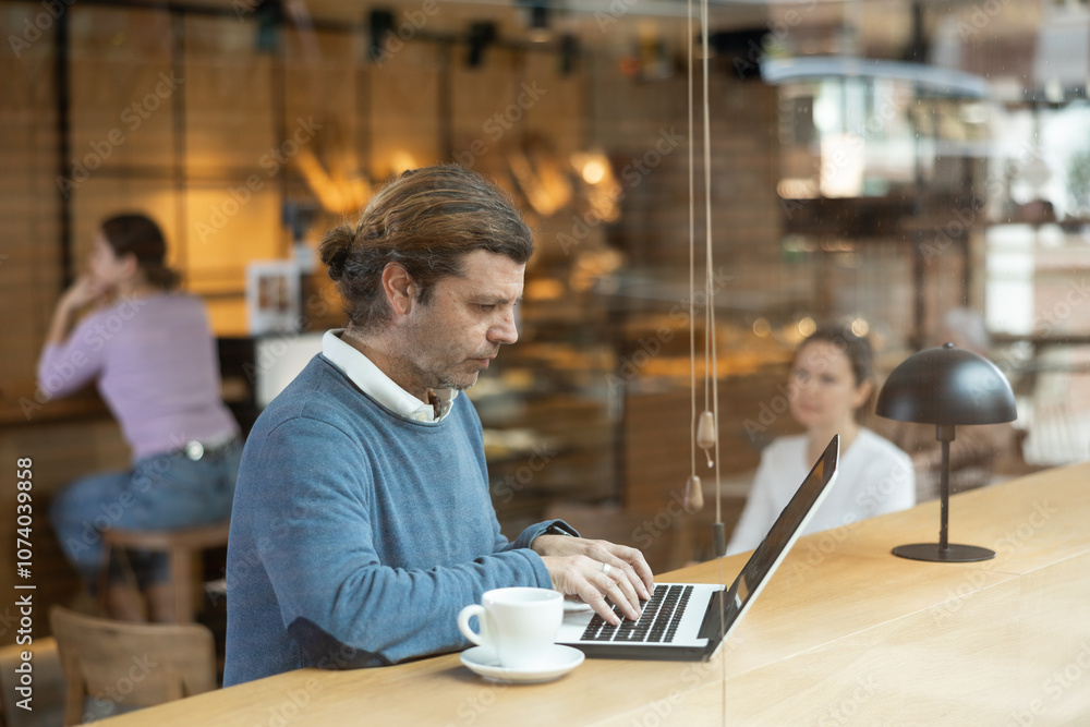 Calm caucasian man sitting in cafe diligently doing his work on laptop Calm caucasian man sitting in cafe diligently doing his work on laptop