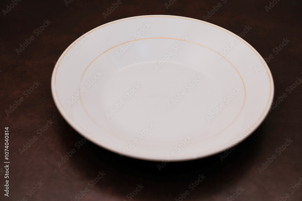 Empty white ceramic plate with orange circle isolated on brown background, eating place setting. Empty white ceramic plate with orange circle isolated on brown background, eating place setting.