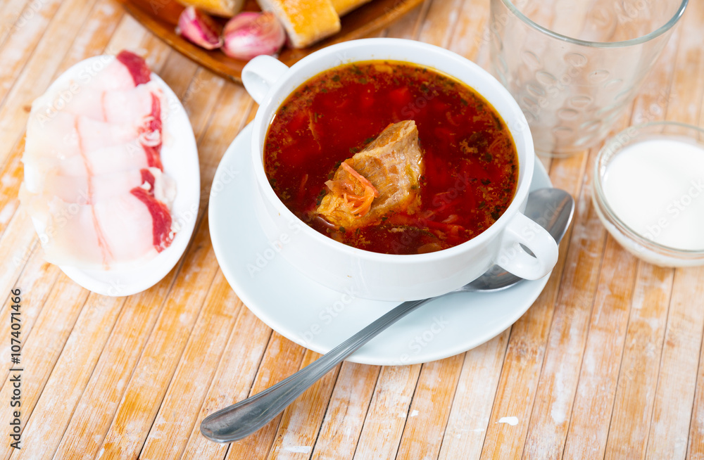Borscht in bowl served on table with salo, garlic and smetana. Borscht in bowl served on table with salo, garlic and smetana.