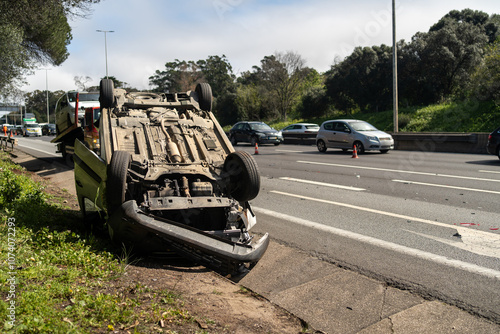 Damaged wrecked car after collision lying upside down on roadside. Busy city street with car rolled over during daytime. Car accident 