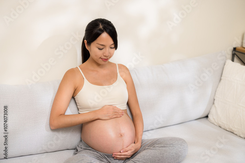 Pregnant woman sit on the sofa and look at her tummy at home