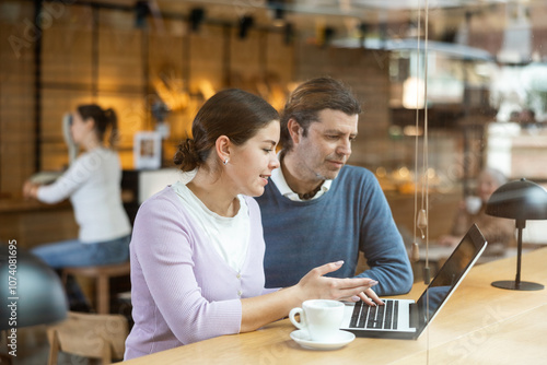 Focused man and woman drinking coffee while working on laptop in cozy cafe