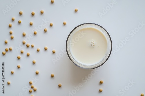 A glass of soy milk and soybeans on a white surface seen from above