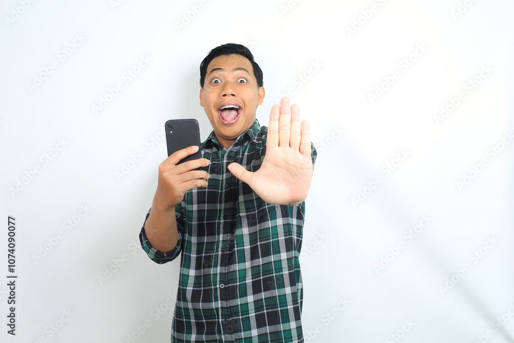 Obraz premium stop, asian man holding smartphone looks surprised isolated on white background, wearing casual green shirt