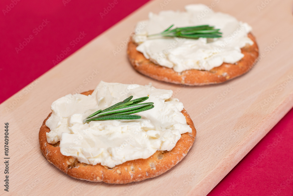 Crispy Cracker Sandwich with Cream Cheese and Rosemary on Wooden Cooking Board on Magenta Background Crispy Cracker Sandwich with Cream Cheese and Rosemary on Wooden Cooking Board on Magenta Background