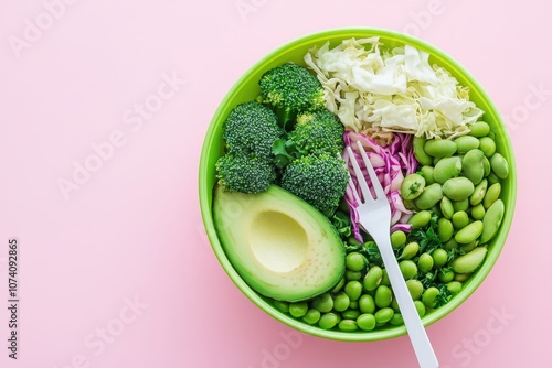 Bird s eye view of a salad bowl featuring avocado edamame cabbage zucchini broccoli and green beans accompanied by a plastic fork on a pink backdrop photo