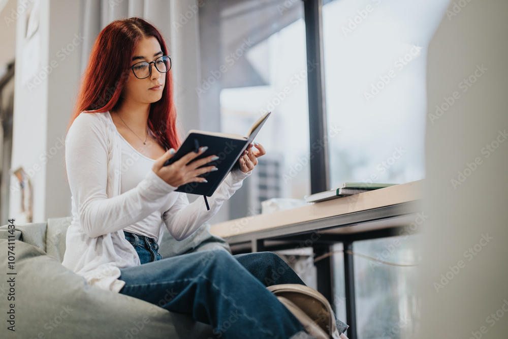 A high school student with glasses concentrating on her studies in a contemporary library. She is sitting on a comfortable seat, engrossed in reading her notebook attentively. A high school student with glasses concentrating on her studies in a contemporary library. She is sitting on a comfortable seat, engrossed in reading her notebook attentively.