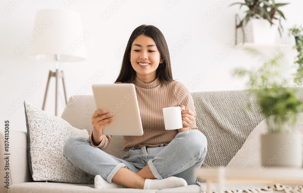 Cheerful girl reading e-book on digital tablet, drinking morning coffee on sofa Cheerful girl reading e-book on digital tablet, drinking morning coffee on sofa