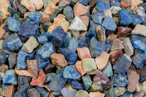 Background showing pile of colorful gemstones with natural pattern, creating beautiful texture. Colorful stones background. Collection of various raw gemstones in different colors and shapes, close up