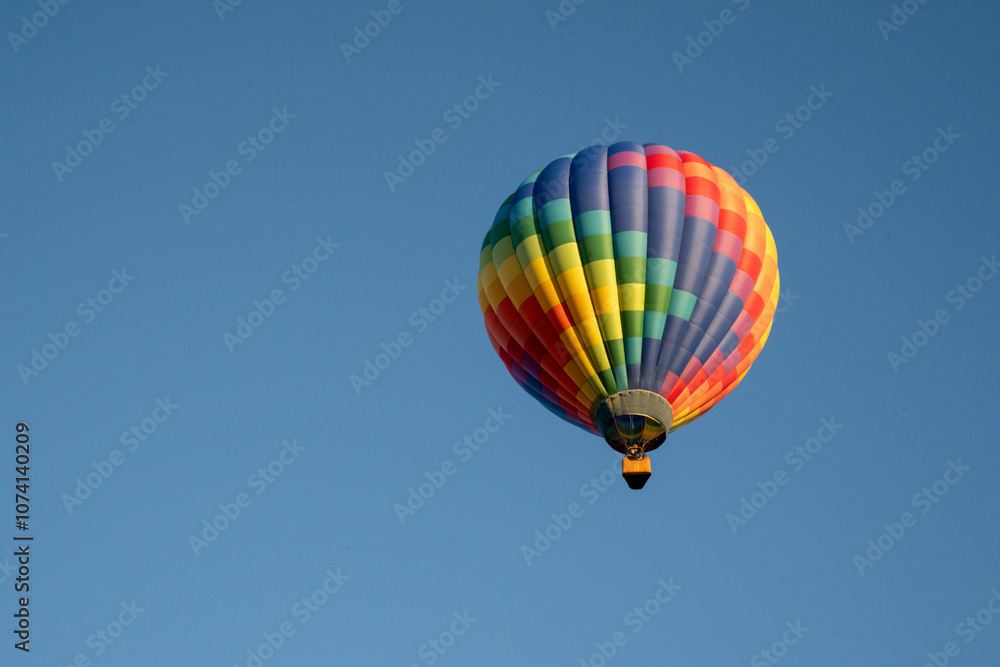 rainbow colored hot air balloon against blue sky with trees rainbow colored hot air balloon against blue sky with trees