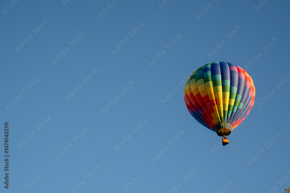 rainbow colored hot air balloon against blue sky with trees rainbow colored hot air balloon against blue sky with trees