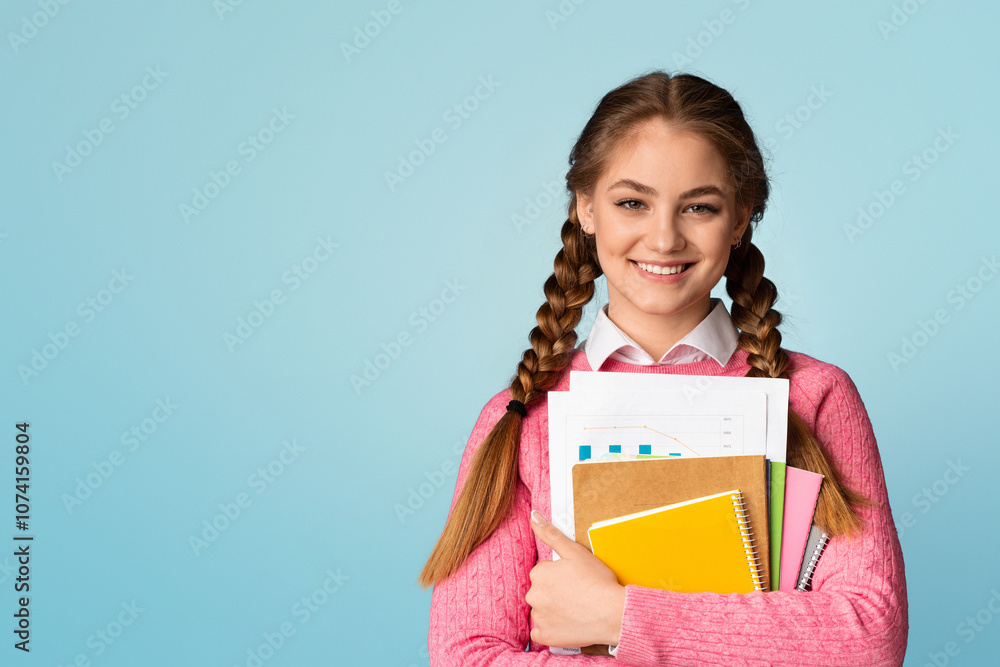 Study on college or school concept. Smiling teenage girl holds notebooks and charts and looks at empty space, isolated on blue background, studio shot Study on college or school concept. Smiling teenage girl holds notebooks and charts and looks at empty space, isolated on blue background, studio shot