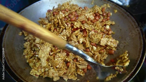 Roasting slices of tempeh, peanuts, and anchovies using a traditional wok
