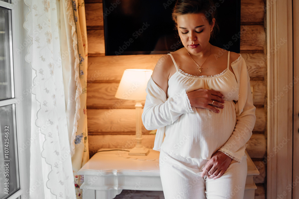 Calm and beautiful young pregnant woman in white pajamas in bedroom Calm and beautiful young pregnant woman in white pajamas in bedroom