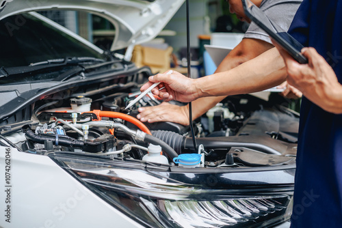 Asian clients engage with a car insurance agent beside a wrecked vehicle. They examine the policy details, assess the damage, and finalize paperwork related to the insurance claim and repairs. photo