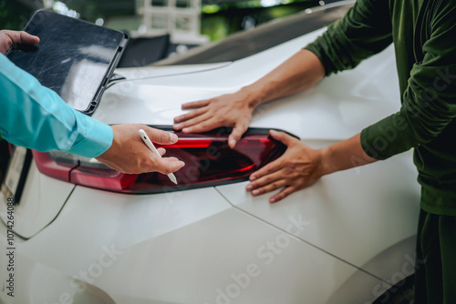 Asian clients engage with a car insurance agent beside a wrecked vehicle. They examine the policy details, assess the damage, and finalize paperwork related to the insurance claim and repairs.