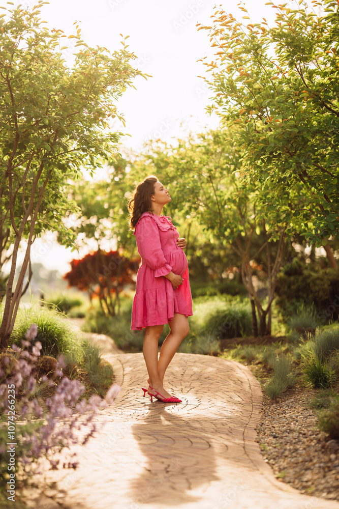 Beautiful and happy pregnant young woman in pink dress on the path in the park Beautiful and happy pregnant young woman in pink dress on the path in the park