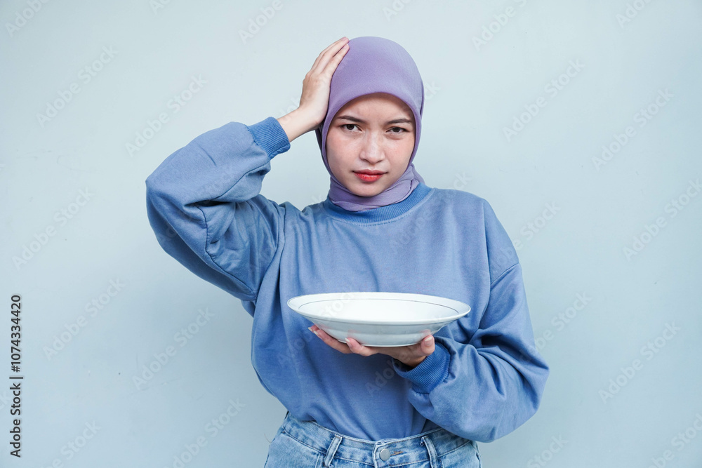 Asian Muslim woman is fasting and hungry and holding cutlery while looking a camera thinking about what to eat with empty plate. Asian Muslim woman is fasting and hungry and holding cutlery while looking a camera thinking about what to eat with empty plate.