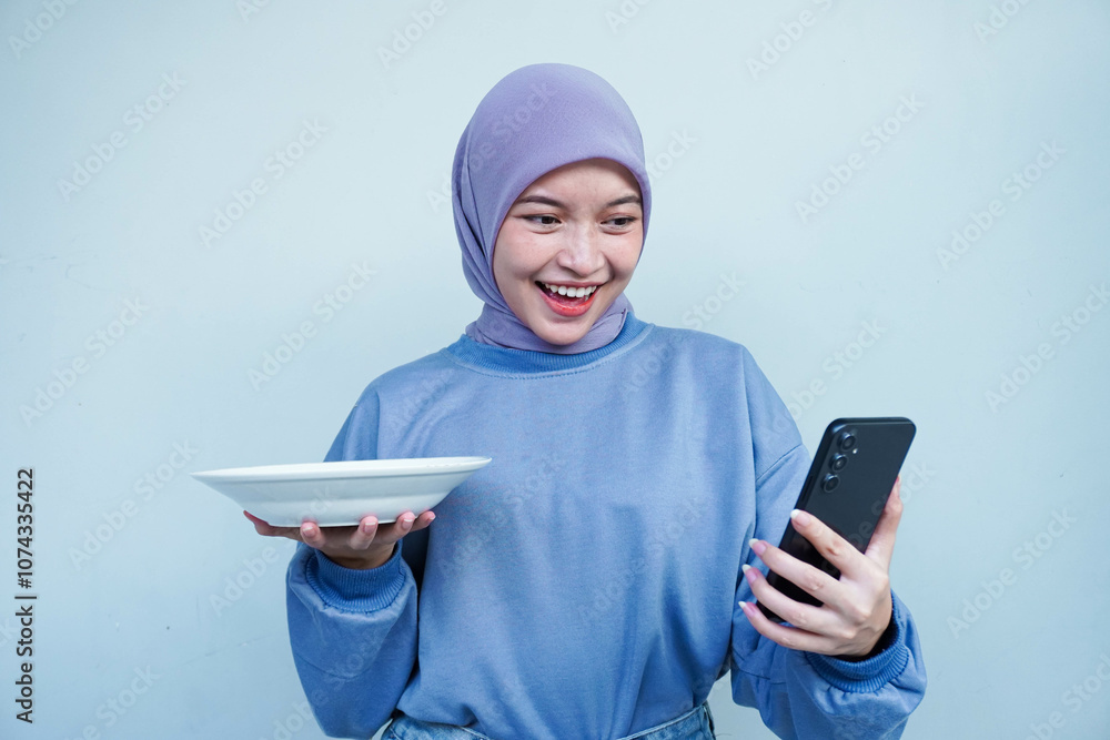 Happiness Asian Muslim woman is fasting and hungry and holding cutlery while looking phone get idea about what to eat. Online food concept. Happiness Asian Muslim woman is fasting and hungry and holding cutlery while looking phone get idea about what to eat. Online food concept.
