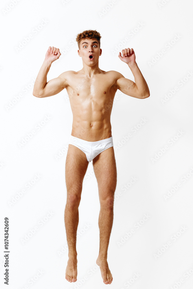 Excited young man jumping in the air, expressing joy and surprise with wide eyes and raised hands. Energy and freedom concept in a bright, minimalist setting. Excited young man jumping in the air, expressing joy and surprise with wide eyes and raised hands. Energy and freedom concept in a bright, minimalist setting.