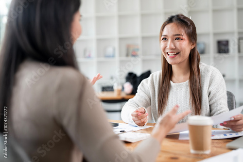 Two females talking and discussing, doing paper work at office desk.