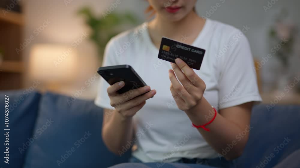 Young woman sitting on a sofa, holding a credit card and shopping online with her smartphone in a relaxed home setting Young woman sitting on a sofa, holding a credit card and shopping online with her smartphone in a relaxed home setting