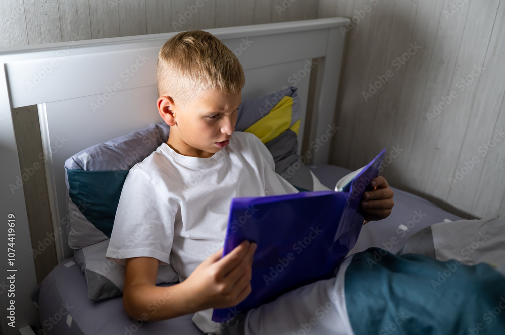 fair-haired teenage boy reading a book before bed fair-haired teenage boy reading a book before bed