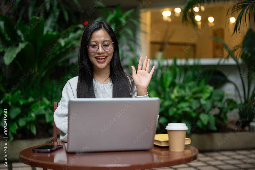 A positive Asian woman has an online meeting or tutors remotely on her laptop from a coffee shop. A positive Asian woman has an online meeting or tutors remotely on her laptop from a coffee shop.