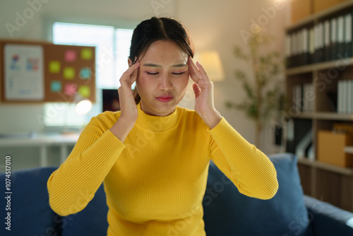 Young woman sitting on the sofa at home office Symptoms include stress, headaches, fatigue and discomfort. The body is weak. Holiday relaxation concept. photo