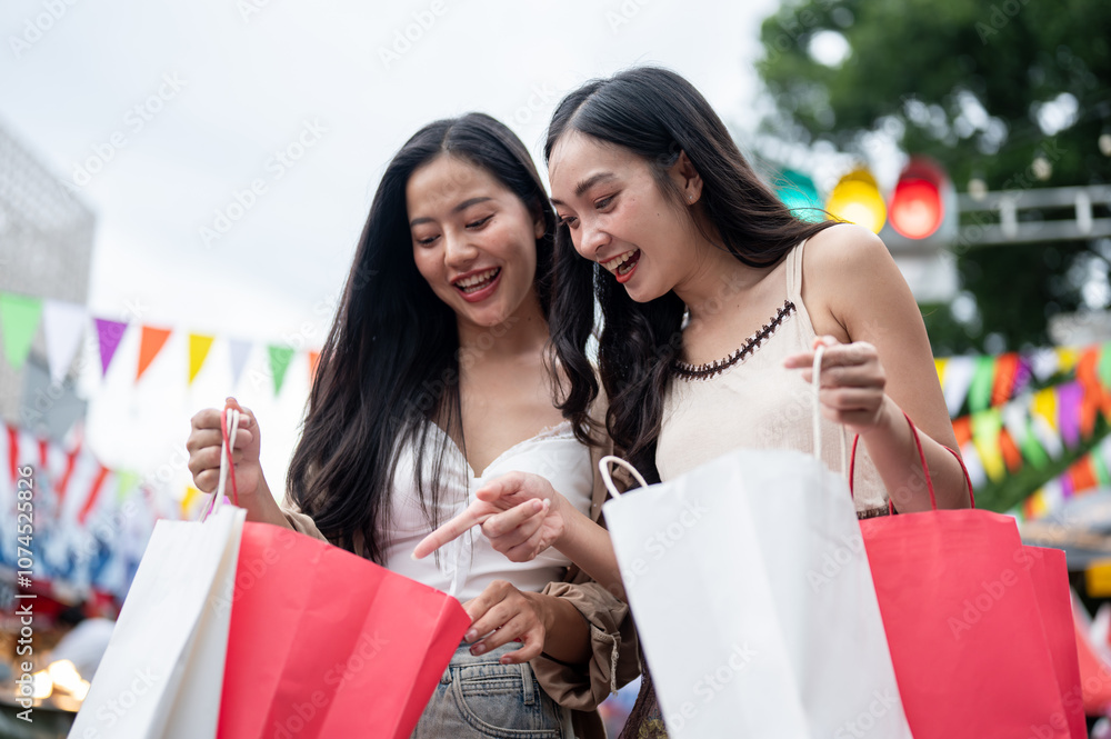 Cheerful Asian female friends are looking inside their shopping bags, enjoying their shopping day. Cheerful Asian female friends are looking inside their shopping bags, enjoying their shopping day.
