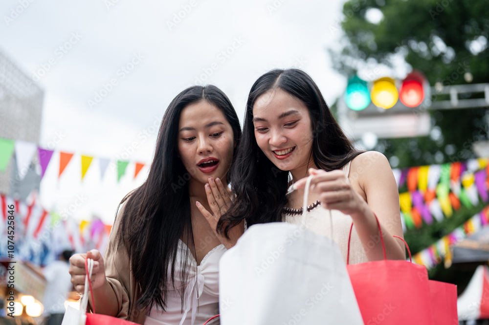 Cheerful Asian female friends are looking inside their shopping bags, enjoying their shopping day. Cheerful Asian female friends are looking inside their shopping bags, enjoying their shopping day.