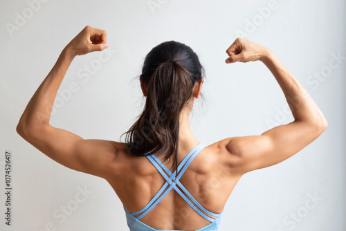 Rear view of strong fit healthy Asian woman with strong muscle and lean body, flexing her back shoulder muscle, concept for fitness gym, sport woman, muscle building, body building, strong and healthy