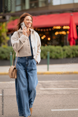 Brunette haired woman walking on the street and using her smartphone