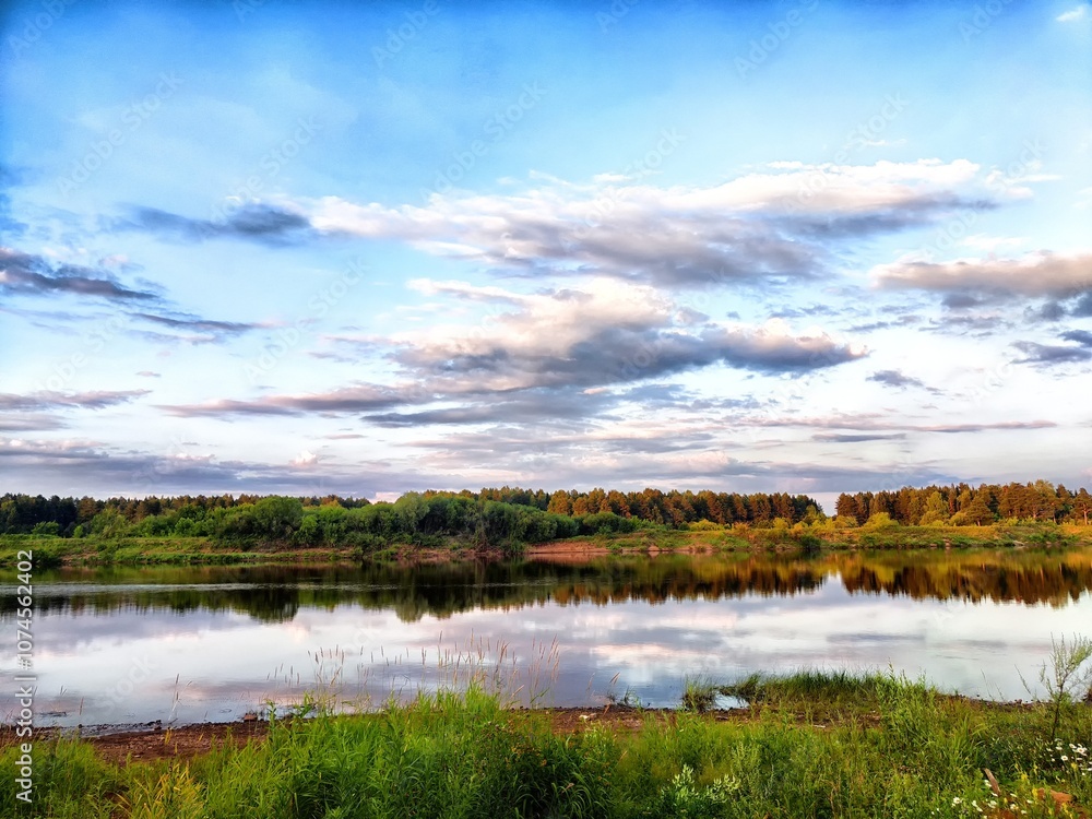 Serene landscape of a calm river reflecting clouds and greenery during sunset Serene landscape of a calm river reflecting clouds and greenery during sunset