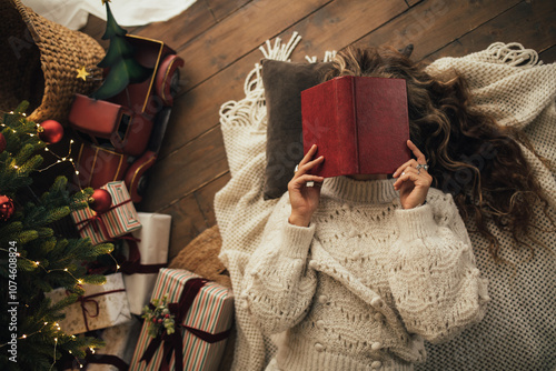 Young woman reading book, lying near Christmas tree in a cozy decorated room. photo