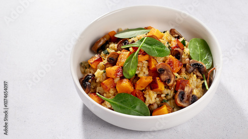 A vegan risotto with roasted pumpkin, mushrooms, and fresh spinach served in a white bowl on a light background