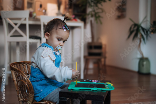 Little Girl Drawing with Tablet and Stylus in Cozy Home Interior photo