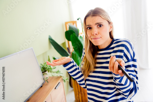 Photo of blonde young woman white screen watch tv shrug shoulders confused dressed striped outfit cozy day light home interior living room photo