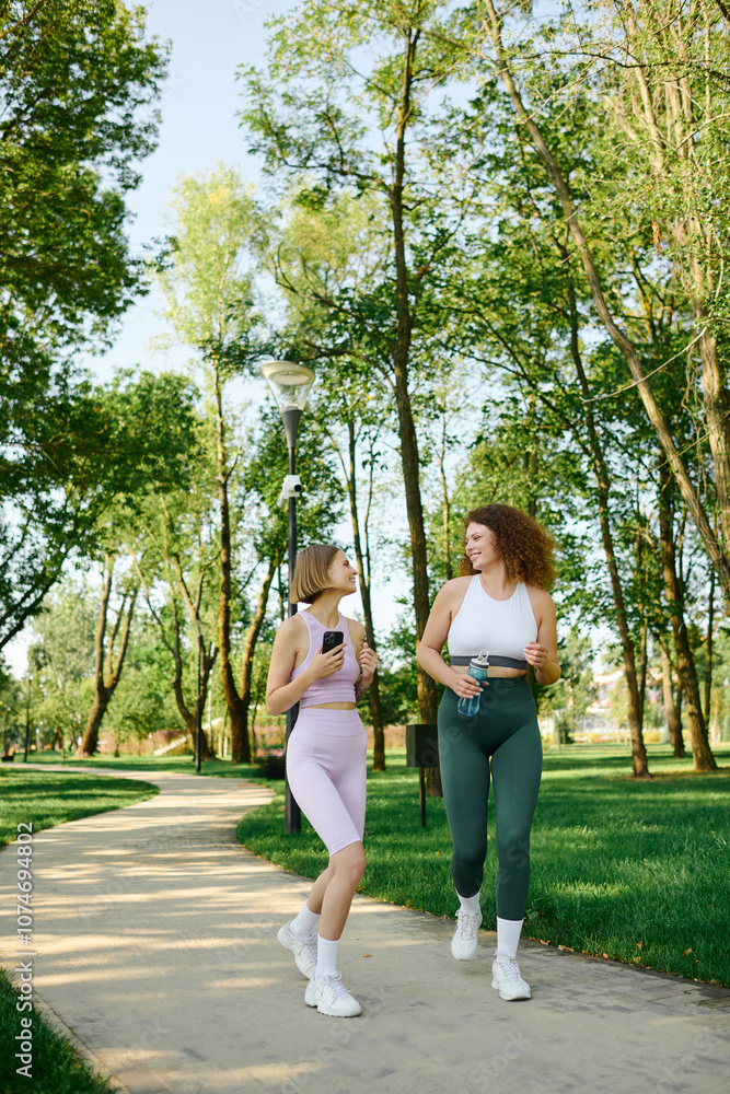 Obraz premium Two women share laughter and conversation while strolling through a vibrant park.