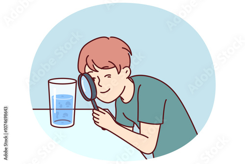 Small boy examines water in glass through magnifying glass, studying chemical composition liquid or looking for microbes. Teenage child curiously studies water, wanting to work in chemical laboratory
