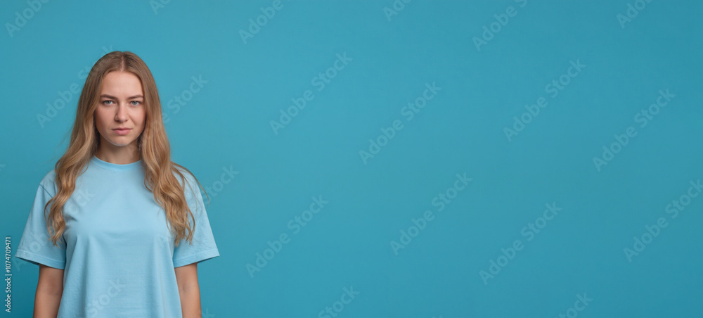 Woman with serious expression wearing light blue shirt against teal background with copy space Woman with serious expression wearing light blue shirt against teal background with copy space