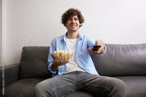 young handsome man watching movies and eating popcorn in a living room #1074711820