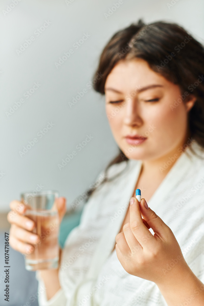 A thoughtful plus size woman at home holds a pill close to her while sipping water. A thoughtful plus size woman at home holds a pill close to her while sipping water.