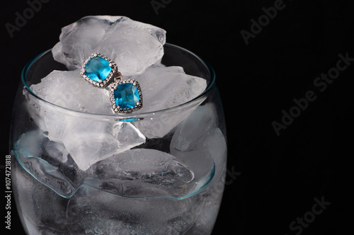  Earrings with blue stones  in a glass with ice and water on black background